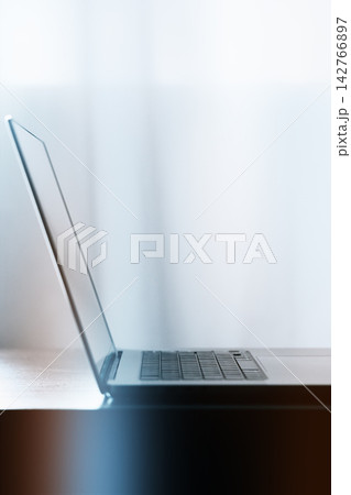 Laptop sits on a table with soft light coming through a window in a quiet room during daytime Laptop sits on a table with soft light coming through a window in a quiet room during daytime 142766897