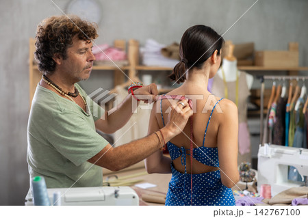 Middle-aged male tailor measuring female client in sewing workshop Middle-aged male tailor measuring female client in sewing workshop 142767100