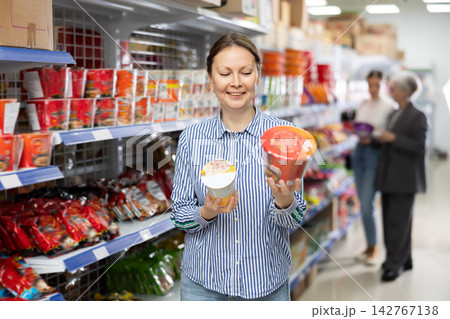 Cheerful woman examining colorful cups of instant noodles at Asian store Cheerful woman examining colorful cups of instant noodles at Asian store 142767138