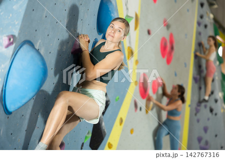 Woman climbs artificial wall bouldering, working out in gym Woman climbs artificial wall bouldering, working out in gym 142767316