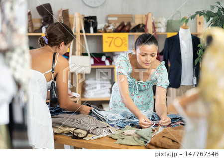 Two young women carefully choosing fashionable jeans or shorts in clothing store 142767346