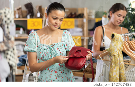 Near rack, Asian woman buys lady handbag, female client in background 142767488