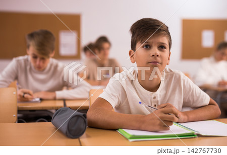 Boy listening to lecturer and writing in notebook in classroom 142767730