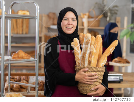 Young Muslim saleswoman displays baguettes while another seller working in background 142767736