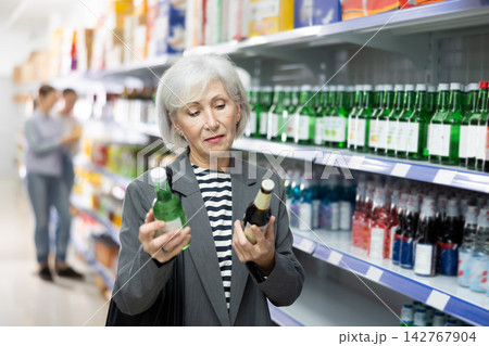 Senior woman customer is thinking about buying spicy and unusual Korean soy wine chum churum. 142767904