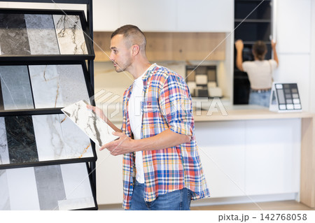 Young man chooses tiles in hardware store Young man chooses tiles in hardware store 142768058