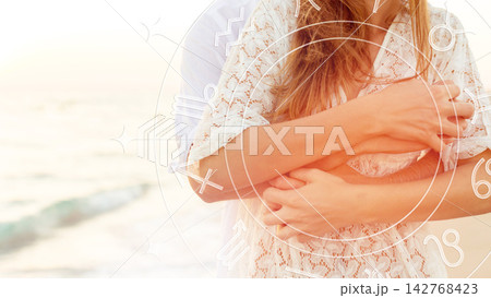 Couple embraces on the beach with astrology zodiac signs in the background during sunset 142768423