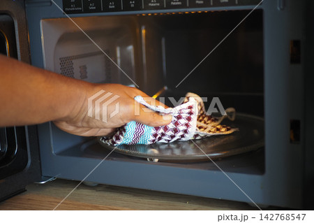 Person placing a cloth into a microwave in a kitchen setting Person placing a cloth into a microwave in a kitchen setting 142768547