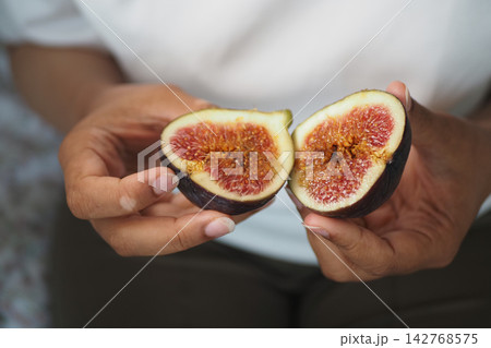Cut fig held by person in hands showing interior details Cut fig held by person in hands showing interior details 142768575