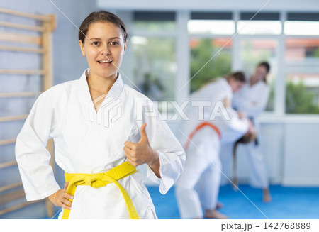 Teenage girl in kimono giving thumbs up in martial arts training room Teenage girl in kimono giving thumbs up in martial arts training room 142768889