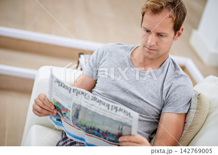 Man, newspaper and relax on couch for peace, calm and comfortable on weekend in living room. Male person, reading and article in apartment, information and rest on sofa in pyjamas for story update 142769005