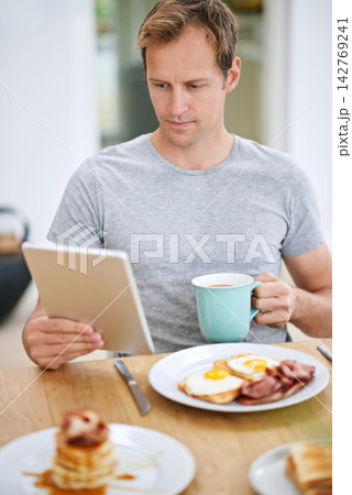 Man, tablet and morning breakfast or reading in home or nutrition meal with coffee, eggs or waffles. Male person, relax and online news in apartment kitchen for relax leisure, streaming or connection Man, tablet and morning breakfast or reading in home or nutrition meal with coffee, eggs or waffles. Male person, relax and online news in apartment kitchen for relax leisure, streaming or connection 142769241