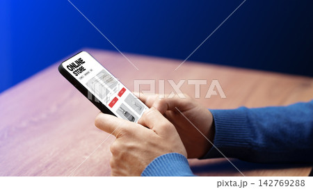 Person uses a smartphone to shop online at an online store displaying different products while sitting at a table 142769288