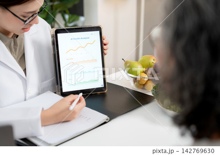 Asian nutritionist showing AI health analysis graph on tablet to senior patient. Asian nutritionist showing AI health analysis graph on tablet to senior patient. 142769630