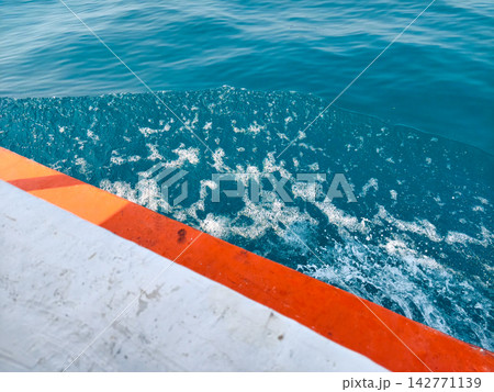 Clear sea water spray beside white and orange boat Clear sea water spray beside white and orange boat 142771139