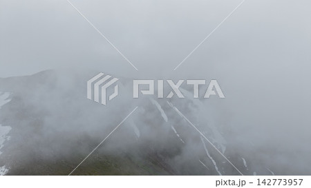 Foggy mountain landscape with snow-capped peaks and low visibility 142773957