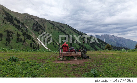 Photographer sitting on bench overlooking green mountains and valley Photographer sitting on bench overlooking green mountains and valley 142774068