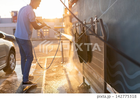 Man washing black floor mats hanging on rack at station 142775318