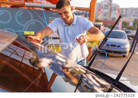 Man wiping wet windshield of car with brown microfiber cloth 142775319