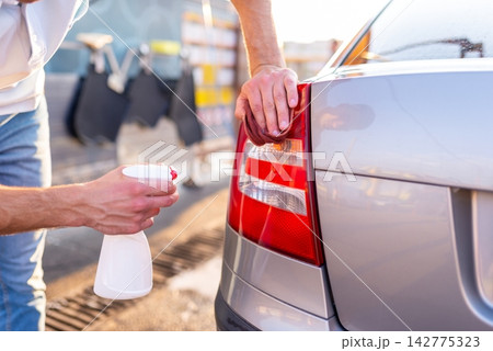 Man spraying detergent and wiping red rear taillight of car 142775323