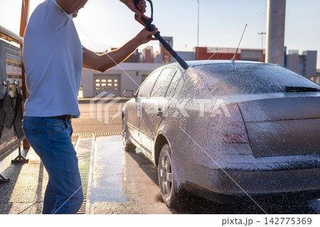 Man spraying water on silver car at self service car wash Man spraying water on silver car at self service car wash 142775369