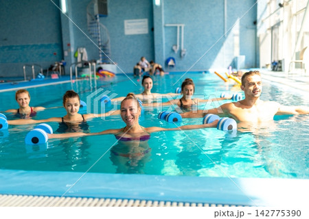 Group exercising with foam dumbbells in pool Group exercising with foam dumbbells in pool 142775390