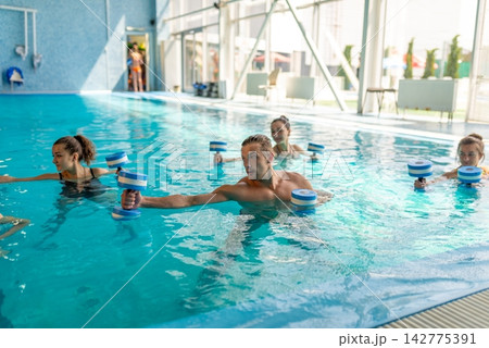 Group exercising with foam dumbbells in pool Group exercising with foam dumbbells in pool 142775391