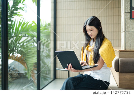 Gen Z Young Woman Using Laptop in Modern Cafe Lounge with Natural Light and Green Plants Gen Z Young Woman Using Laptop in Modern Cafe Lounge with Natural Light and Green Plants 142775752