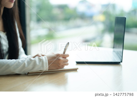 Closeup Woman Studying with Laptop and Notebook at Wooden Desk in Modern Interior Closeup Woman Studying with Laptop and Notebook at Wooden Desk in Modern Interior 142775798