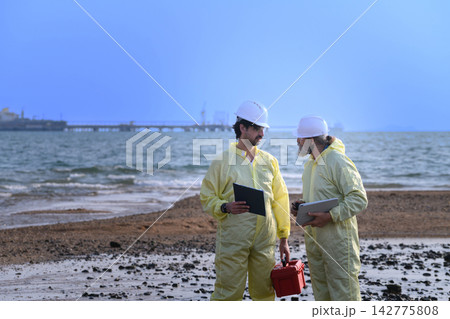 Environmental engineers inspecting coastal area near industrial tanker ship Environmental engineers inspecting coastal area near industrial tanker ship 142775808