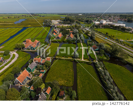 High angle wide horizontal aerial drone photograph of Zaanse Schans historic village, green wooden houses, drainage canals, footbridges, and polder meadows in Zaandam, North Holland, Netherlands 142776142