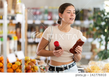 Girl hold bottle, choose and buy ketchup in store 142776910