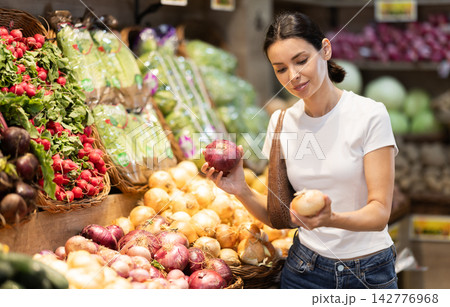 Girl client near vegetable stand in store choose onion 142776968