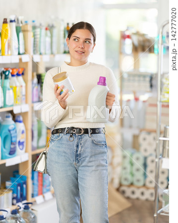 Girl reads label, choose and compare liquid detergent and powdered detergent 142777020