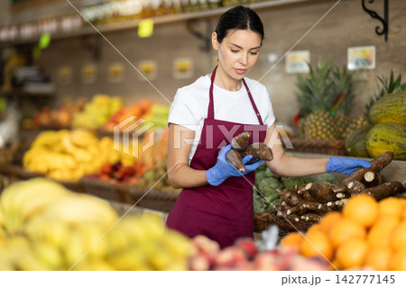 Girl shop seller add cassava goods on display case in vegetable store Girl shop seller add cassava goods on display case in vegetable store 142777145