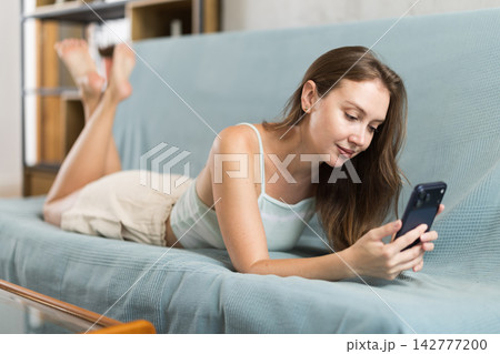 Adult woman scrolling smartphone on sofa 142777200