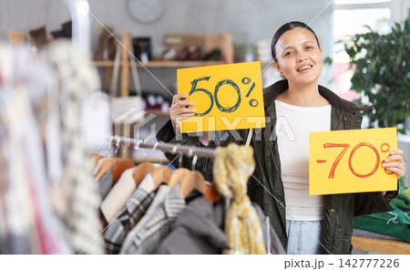 Asian woman holds yellow poster informing about discounts in store Asian woman holds yellow poster informing about discounts in store 142777226