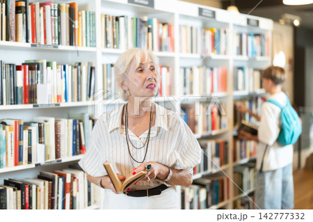 Happy senior woman choosing books in large bookstore Happy senior woman choosing books in large bookstore 142777332