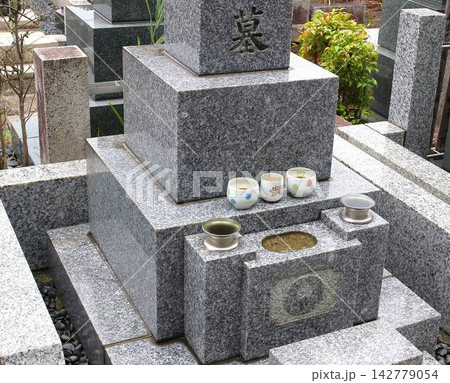「墓」と刻まれた御影石の和型墓石と水玉模様の湯呑み供物 142779054