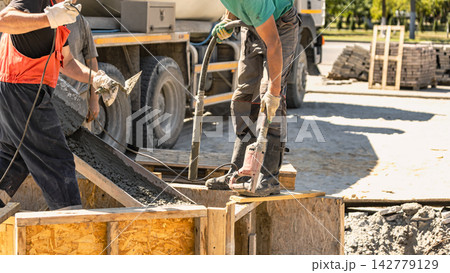 Concrete is being poured into forms to create a solid foundation at a construction site. The workers are using a concrete pump and molds Concrete is being poured into forms to create a solid foundation at a construction site. The workers are using a concrete pump and molds 142779129