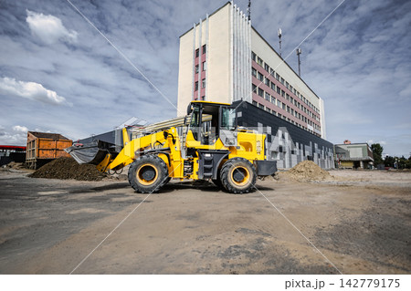 A loader is working at a construction site near a large building, moving dirt and materials for various landscaping tasks 142779175