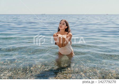 Woman, swimsuit, sea Young woman blowing kiss standing waist-deep in clear ocean water on sunny summer vacation Woman, swimsuit, sea Young woman blowing kiss standing waist-deep in clear ocean water on sunny summer vacation 142779270