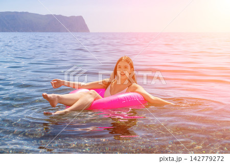 Woman floating ocean, young girl relaxing happily on vibrant pink swim ring during summer holiday Woman floating ocean, young girl relaxing happily on vibrant pink swim ring during summer holiday 142779272