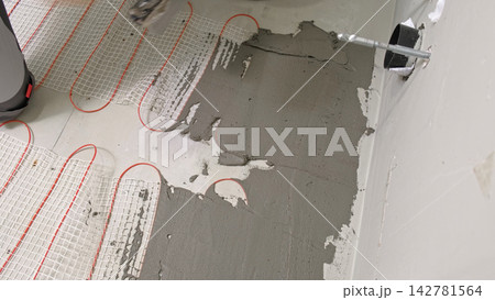Worker installing electric underfloor heating system mat. Underf 142781564