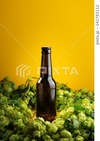 Amber glass bottle of craft beer surrounded by fresh green hops flowers with yellow background Amber glass bottle of craft beer surrounded by fresh green hops flowers with yellow background 142783112
