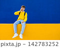 Young student talking on phone sitting on colorful wall 142783252