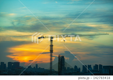 Towering construction crane silhouetted against a vibrant sunset sky over city Towering construction crane silhouetted against a vibrant sunset sky over city 142783418