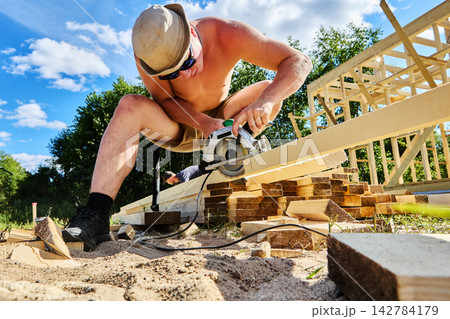 Cutting lumber with circular saw, young worker operates power tool during construction of structural frame. Cutting lumber with circular saw, young worker operates power tool during construction of structural frame. 142784179