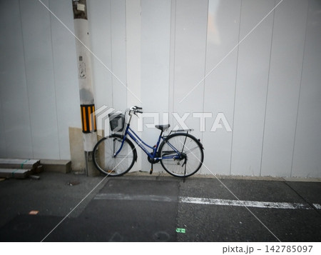 街中の電柱脇に置かれた青色のママチャリと工事現場の仮囲い 街中の電柱脇に置かれた青色のママチャリと工事現場の仮囲い 142785097