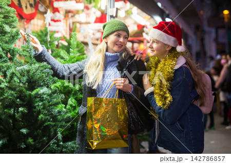Mother with teenager daughter choose christmas tree at street fair Mother with teenager daughter choose christmas tree at street fair 142786857